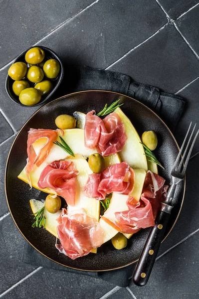 Prosciutto ham and melon salad in a plate. Black background. Top view.