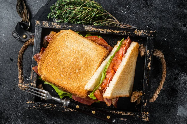 Homemade toasted BLT sandwich with bacon, tomato and lettuce in wooden tray. Black background. Top view.