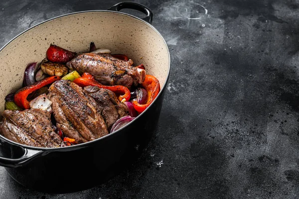 Braised slow cooked lamb shank in red wine sauce with vegetables in cooking pot. Black background. Top view. Copy space.