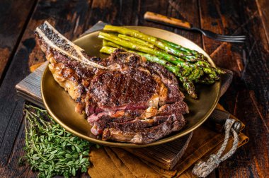 Sliced Grilled Cowboy or rib eye with bone beef steak, roasted asparagus in a plate. Wooden background. Top view.