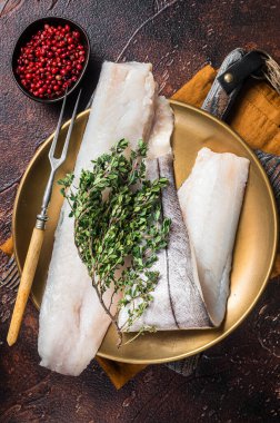 Beyaz balık filetosu, biberiye ve kekik tabağında çiğ mezgit balığı. Karanlık arka plan. Üst görünüm.