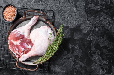 Raw Free range duck legs in a steel tray with thyme. Black background. Top view. Copy space.