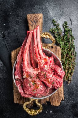 Lamb mutton chop steak, raw meat cutlet in a skillet with herbs. Black background. Top view.