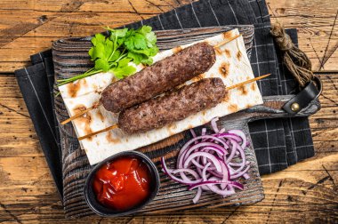 Traditional middle east kefta, kofta kebab from ground beef and lamb meat grilled on skewers served with flatbread and onion. Wooden background. Top view.