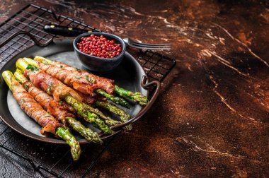 Baked Prosciutto wrapped green asparagus. Dark background. Top view. Copy space.