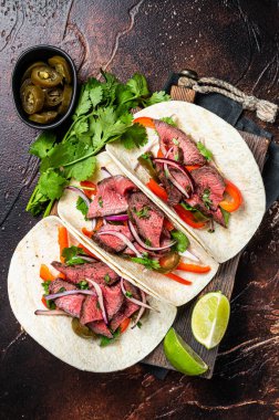 Carne Asada Tacos with grilled steak, green sauce, jalapenos and onion, Mexican food. Dark background. top view.
