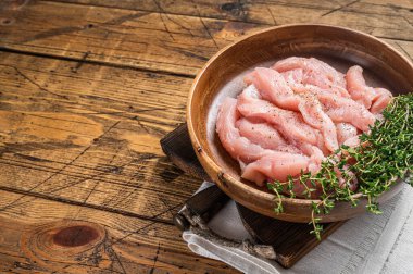 Sliced raw chicken, turkey breast meat in a wooden plate with thyme. Wooden background. Top view. Copy space.
