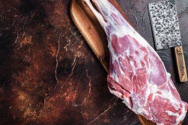 Raw whole lamb leg thigh on butcher board. Dark background. Top view. Copy space.