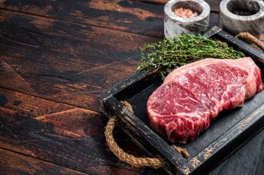 Prime raw new york beef meat steak with herbs ready for cooking. Wooden background. Top view. Copy space.