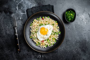 Fried rice with chicken, egg and vegetables in a plate. Black background. Top view.