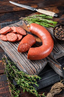 Kesme tahtasının üzerinde otlarla dilimlenmiş sucuk eti sosisi. Ahşap arka plan. Üst görünüm.