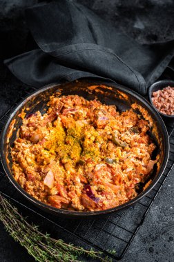 Turkish Menemen omelet in a frying pan. Black background. Top view.
