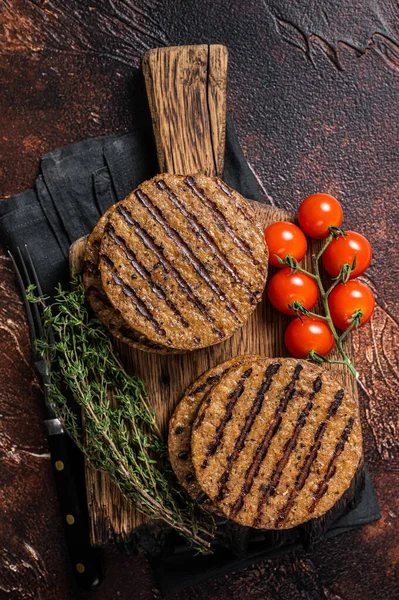 BBQ Grilled plant based meat burger patties, vegan cutlets on wooden board with herbs. Dark background. Top view.