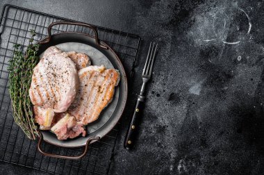 Grilled delicious pork chop steaks with herbs and spices. Black background. Top view. Copy space.