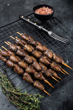 Grilled shish kebab with chicken hearts on a grill. Black background. Top view.