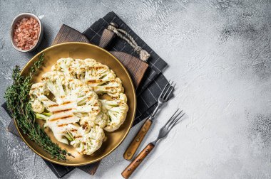 Grilled cauliflower steak with thyme and spices in a plate. White background. Top view. Copy space.