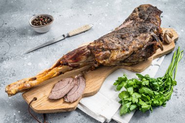 Whole roast mutton lamb leg with spices on a wooden board. Gray background. Top view.