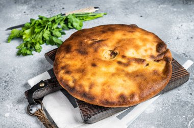Ossetian pie with beef meat and herbs on wooden board. Gray background. Top view.