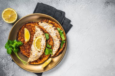 Turkish lahmacun pizza with mince meat and tomatoes on a plate with parsley and lemon. White background. Top view. Copy space.