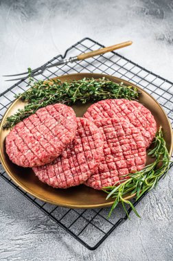 Raw minced beef burgers with spices on steel plate with rosemary and thyme. White background. Top view.
