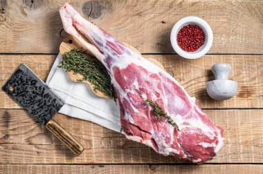 Butcher board with Raw lamb mutton leg with herbs. Wooden background. Top view.