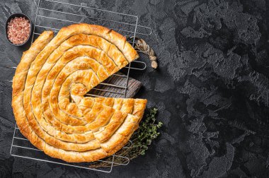 Turkish Tepsi Boregi, Round Borek cheese pie on kitchen board. Black background. Top view. Copy space.