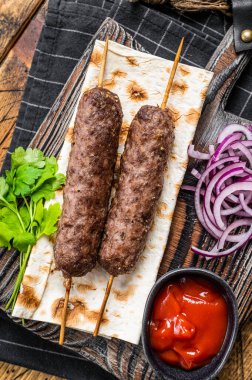 Traditional middle east kefta, kofta kebab from ground beef and lamb meat grilled on skewers served with flatbread and onion. Wooden background. Top view.