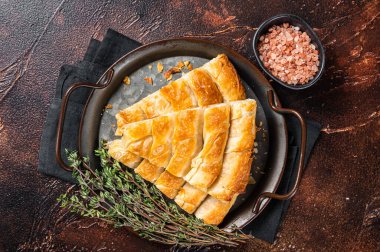 Slices of baked Round Borek cheese pie in kitchen tray with herbs. Dark background. Top view.