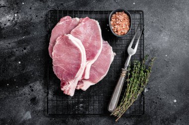 Raw pork cutlet chop steak for fry on pan with herbs. Black background. Top view.