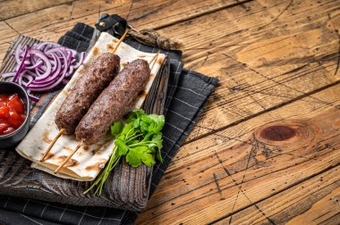 Traditional middle east kefta, kofta kebab from ground beef and lamb meat grilled on skewers served with flatbread and onion. Wooden background. Top view. Copy space.