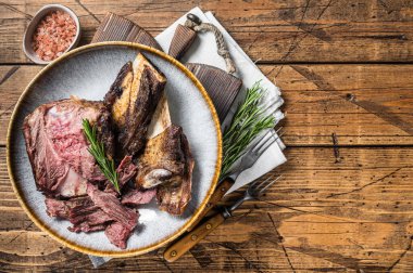 Roasted veal beef short ribs in plate with rosemary. Wooden background. Top view. Copy space.