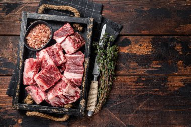 Uncooked Raw diced cubes of lamb meat in wooden tray with salt and thyme. Wooden background. Top view. Copy space.
