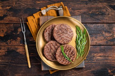 Grilled burger beef meat patty with herbs and spices on steel plate. Wooden background. Top view.