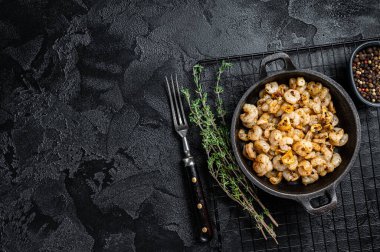 Roasted Shrimps with garlic, olive oil and spices in a skillet. Black background. top view. copy space.