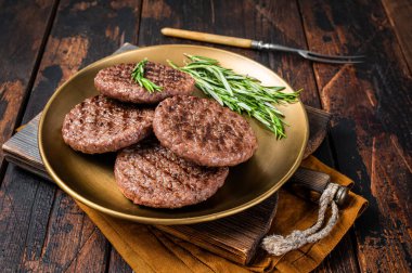 Grilled burger beef meat patty with herbs and spices on steel plate. Wooden background. Top view.