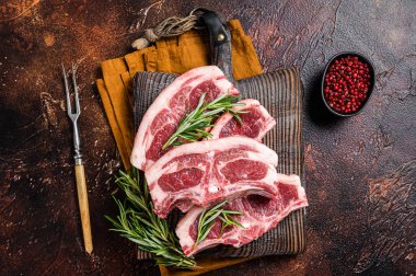 Raw fresh saddle of lamb mutton with herbs and spices on butcher board. Dark background. Top view.