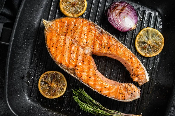 Salmon Fish Steak grilled on a grill pan with herbs. Black background. Top view.