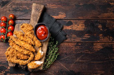 Crispy fried Breaded chicken strips, breast fillet meat with tomato ketchup on a plate. Wooden backgrund. Top view. Copy space.