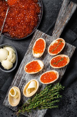 Tahtada kırmızı havyarlı tart, tereyağı ve kekik. Siyah arka plan. Üst görünüm.