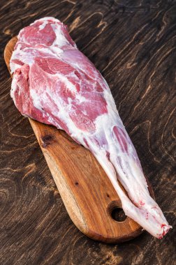 Mutton meat. Raw whole lamb leg thigh on butcher board. Wooden background. Top view.
