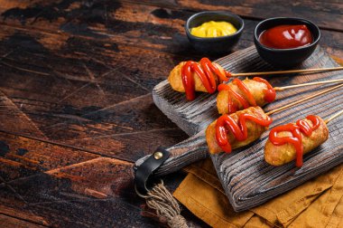 Mini Deep fried corn dogs with mustard and ketchup on wooden board. Wooden background. Top view. Copy space.