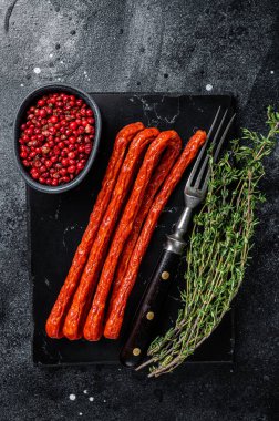 Smoked kabanos sausages with herbs on marble board. Black background. Top view.