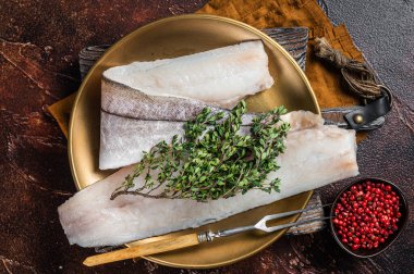 Beyaz balık filetosu, biberiye ve kekik tabağında çiğ mezgit balığı. Karanlık arka plan. Üst görünüm.