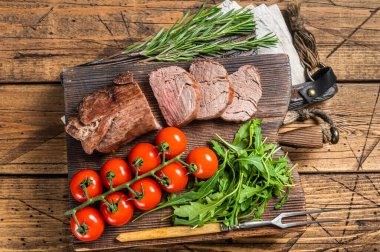 Kızarmış dana filetosu, ahşap tahtada dilimlenmiş biftek ve garnitür. Ahşap arka plan. Üst görünüm.