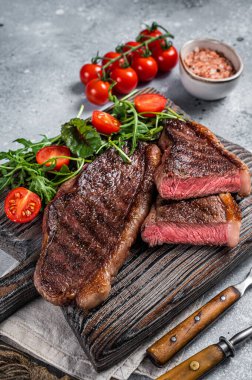 Kızarmış sığır budu ya da ahşap tahtada salatalı sığır etli biftek. Gri arka plan. Üst görünüm.