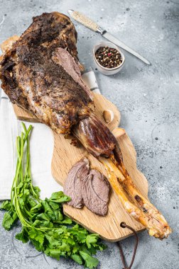 Whole roast mutton lamb leg with spices on a wooden board. Gray background. Top view.