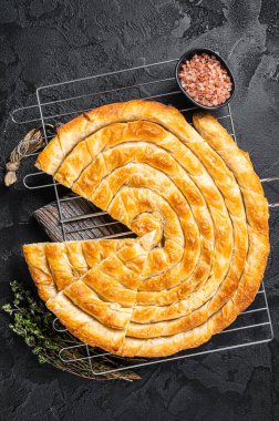 Turkish Tepsi Boregi, Round Borek cheese pie on kitchen board. Black background. Top view.