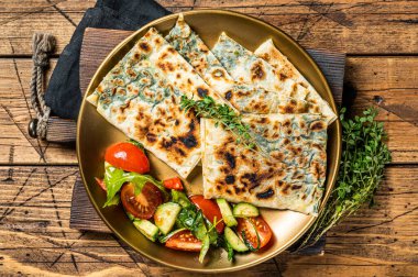 Gozleme flatbread with greens and vegetable salad on garnish. Wooden background. Top view.