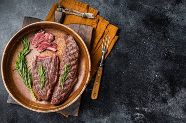 Fried sirloin flap or flank beef steak with herbs in a wooden plate. Black background. Top view. Copy space.