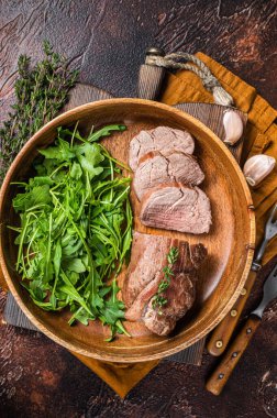Juicy tenderloin Steak, sliced Roast beef in wooden plate with arugula. Dark background. Top view.